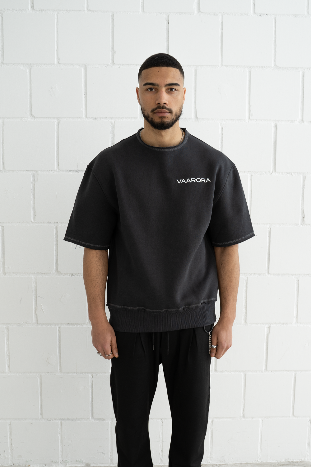 Front view of a male model wearing the black Vaarora Cato Heavy Tee showcasing the raw-edge neckline and minimalist logo print