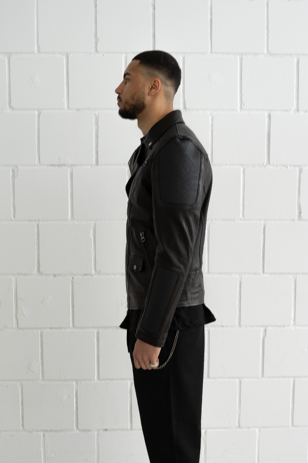Side profile of a male model wearing the black Vaarora Manu biker jacket highlighting the textured leather sleeve panels