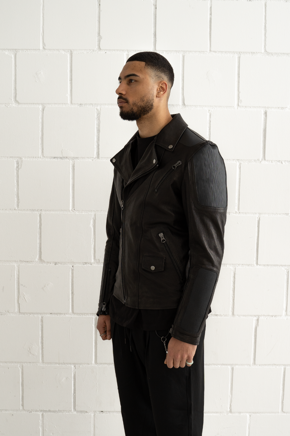 Angled front view of the Vaarora black leather biker jacket showing the asymmetrical zipper and silver hardware