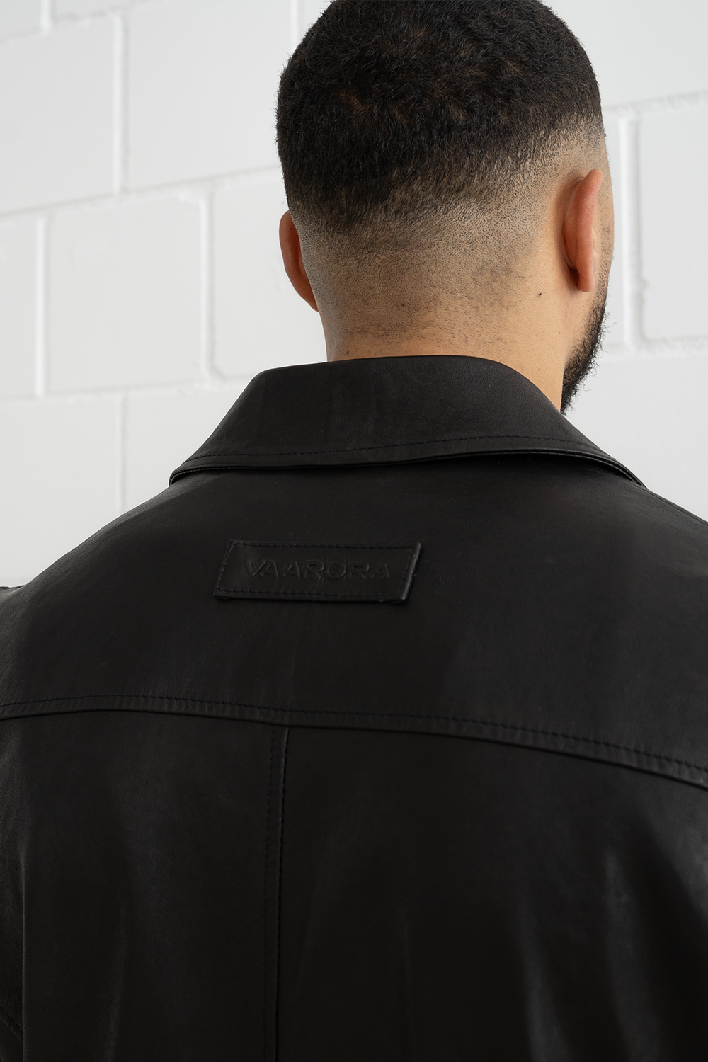 Close-up of the vintage-style embossed Vaarora logo patch on the back neck of the black Manu biker jacket
