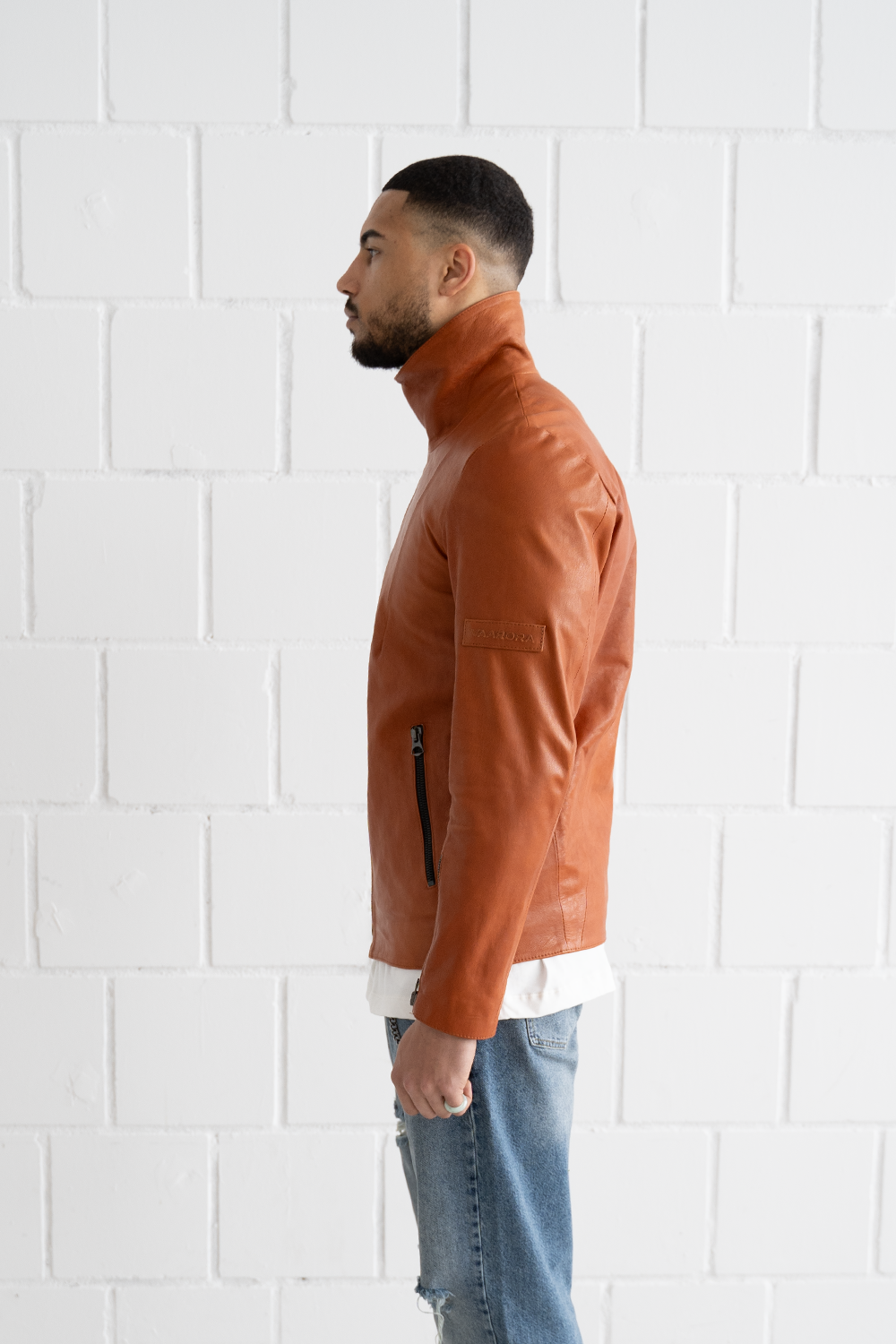 Side view of the Vaarora camel leather jacket showcasing the stand-up collar, sleeve zipper, and embossed logo patch