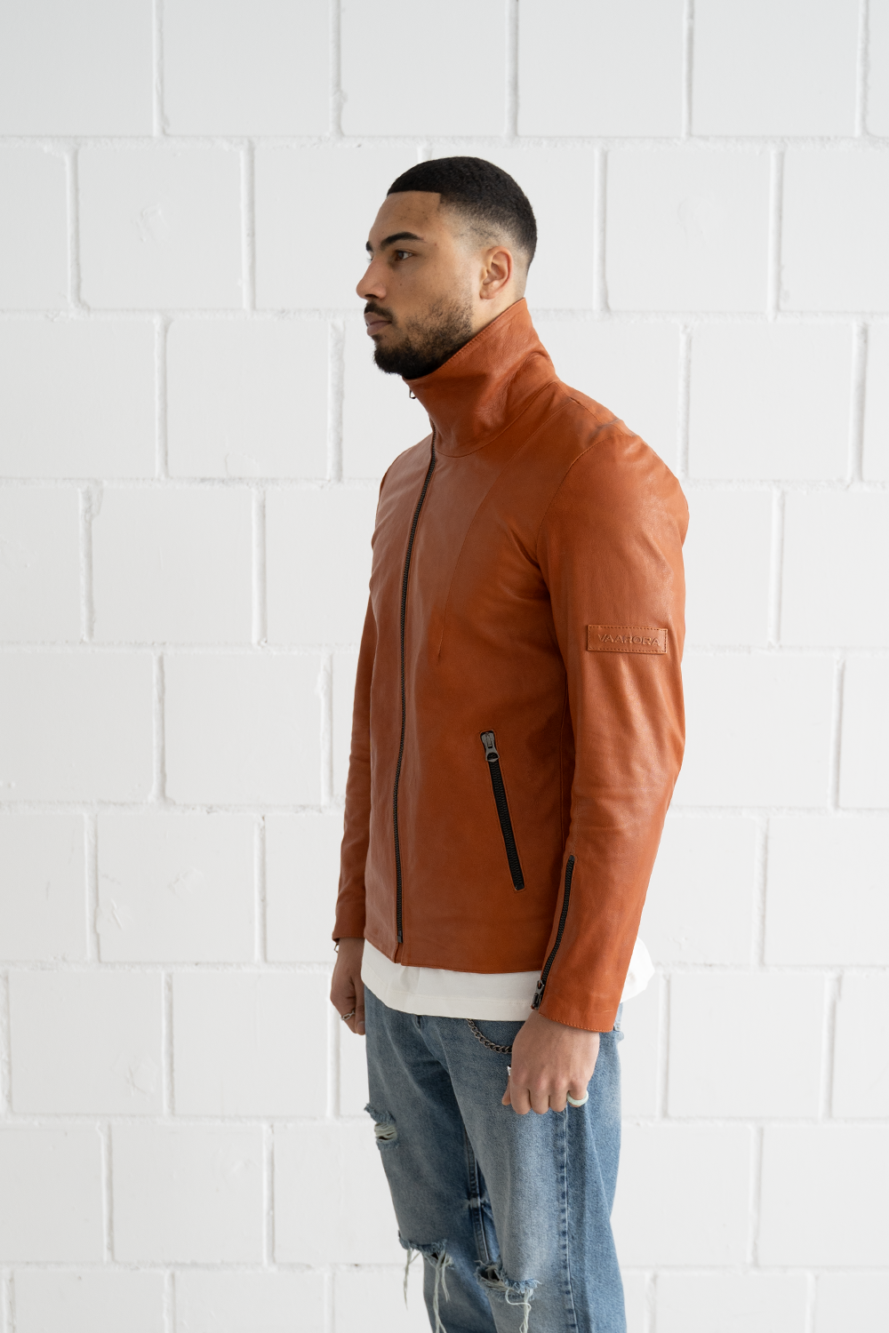 Side view of the Vaarora camel leather jacket showcasing the stand-up collar, sleeve zipper, and embossed logo patch