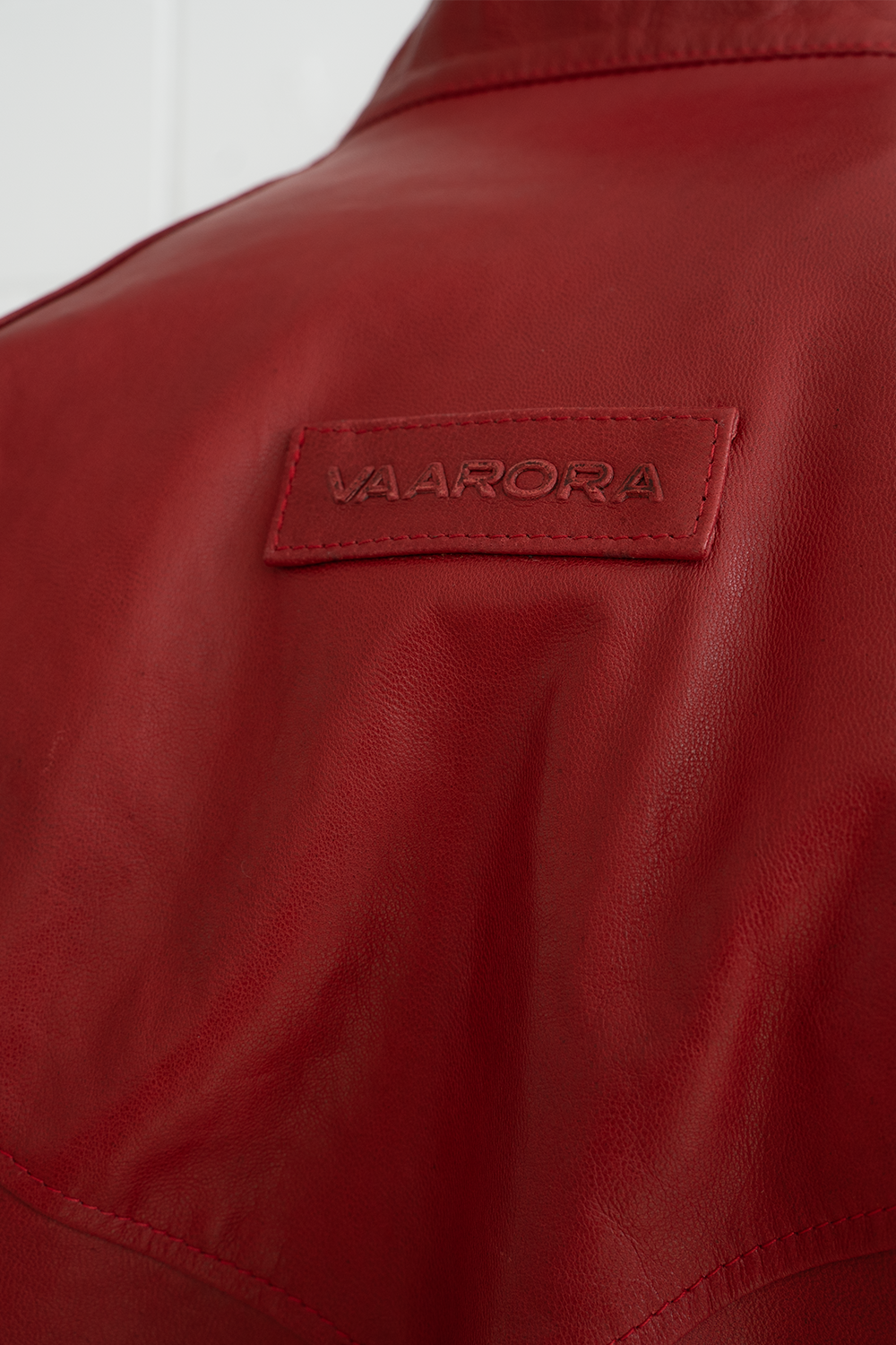 Close-up of the vintage-style embossed Vaarora logo patch on the back of the red Vittorio premium leather jacket